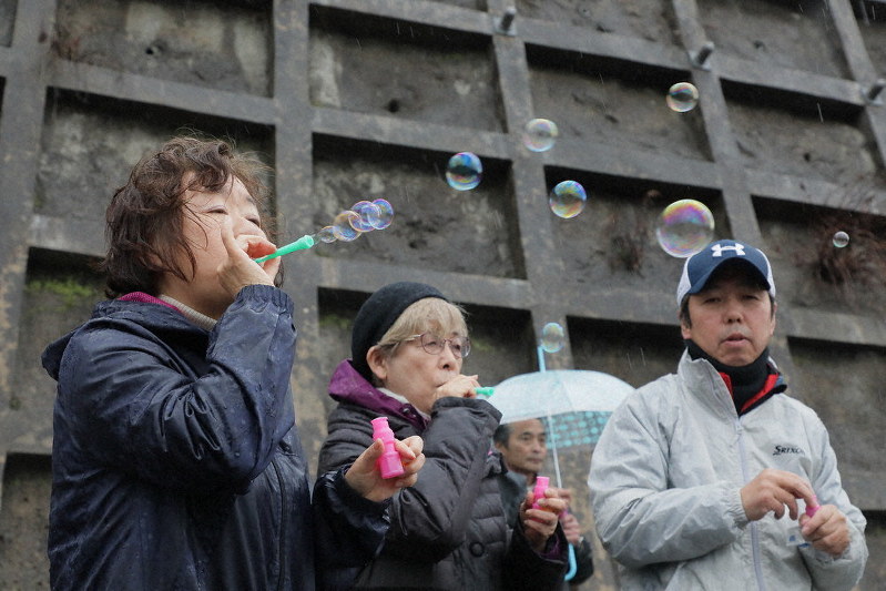 七十七銀行旧女川支店跡地近くのモニュメントを訪れた美谷島邦子さん(中央)とシャボン玉を飛ばす田村孝行さん(右)、妻弘美さん=宮城県女川町で2020年3月10日午後3時21分、和田大典撮影