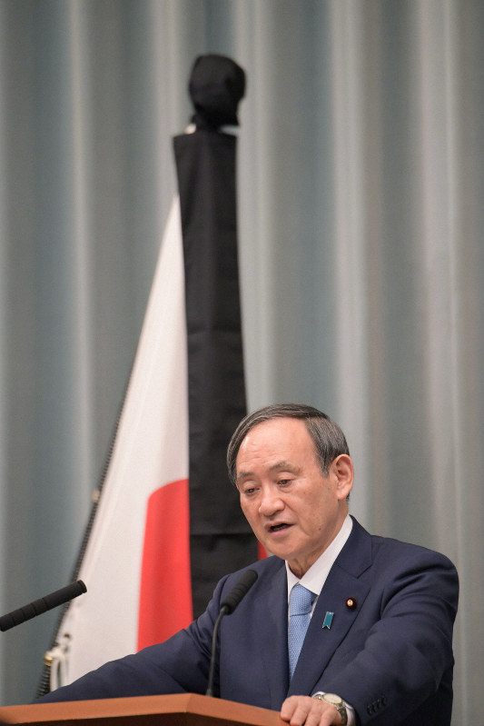 記者会見で質問に答える菅義偉官房長官。奥は東日本大震災の犠牲者を哀悼の意をあらわす弔旗=首相官邸で2020年3月11日午前11時21分、川田雅浩撮影