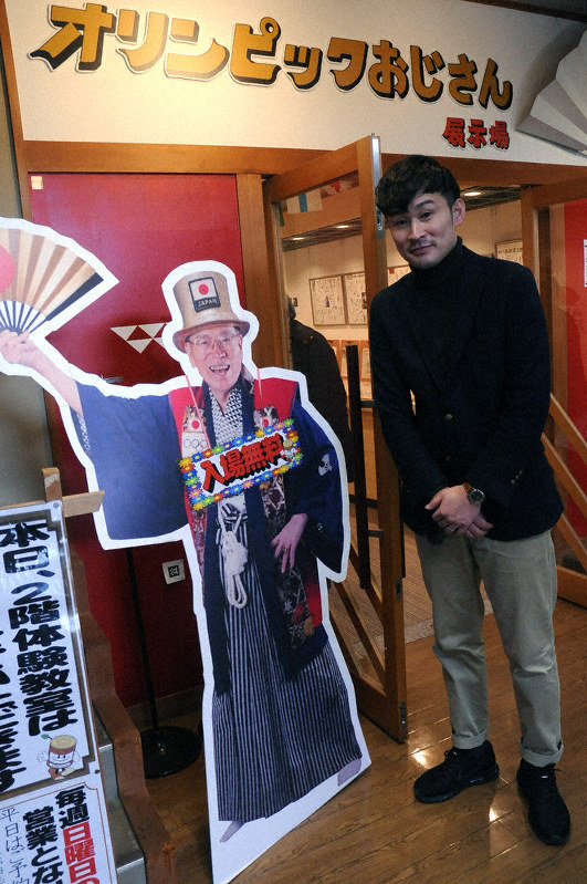 山田直稔さんのパネルの横で「ぜひ、お越し下さい」と呼び掛ける「いなみ木彫りの里」営業部長で「道の駅井波」駅長の江尻大朗さん=南砺市北川で、柳澤一男撮影