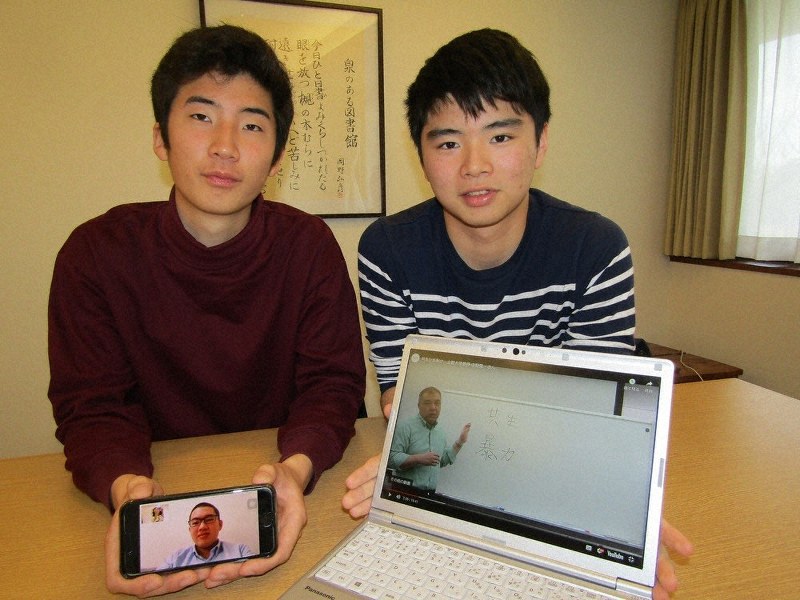 サイトの画像を示す小林多治生さん(右)と、川嶋一さん。スマートフォンに映っているのは、名古屋市の自宅に戻っている幸田良佑さん=東久留米市で