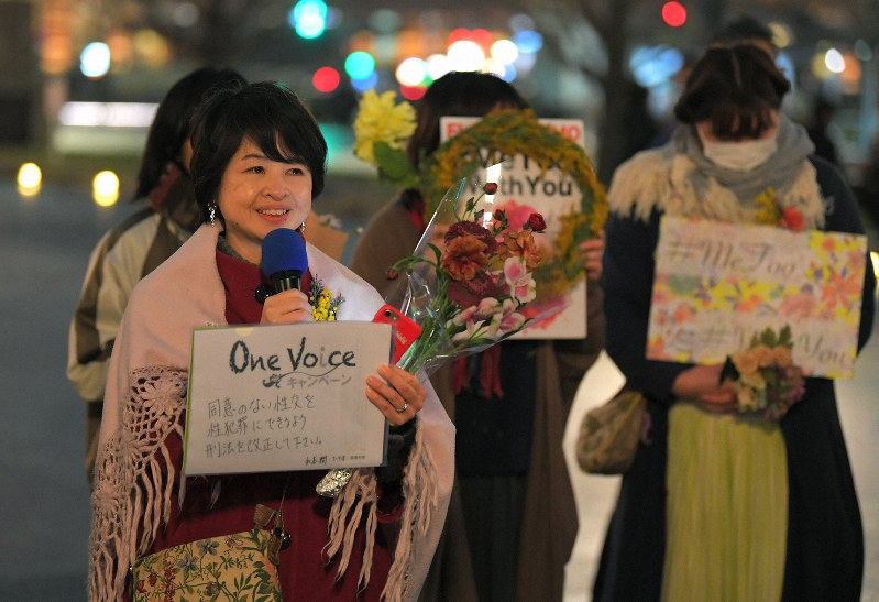 新型コロナウイルスの影響でインターネット中継となったフラワーデモで「One Voiceキャンペーン」と書いた紙を掲げて思いを伝える山本潤さん(左)ら=東京都千代田区で2020年3月8日午後6時12分、手塚耕一郎撮影