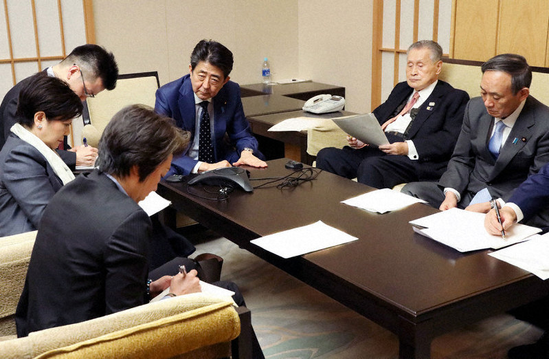 国際オリンピック委員会のバッハ会長と電話協議する安倍晋三首相(右から3人目)、大会組織委員会の森喜朗会長(同2人目)、東京都の小池百合子知事(左手前から2人目)ら=首相公邸で24日午後8時すぎ(内閣広報室提供)