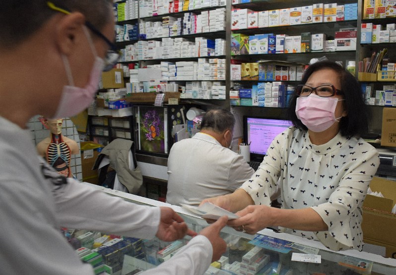 マスクを買い求める市民に応対する薬局店主。奥の男性はパソコンに健康保険カードの番号を打ち込み、マスクの購入履歴を確認している=台北市中山区で2020年3月8日午前9時10分、福岡静哉撮影