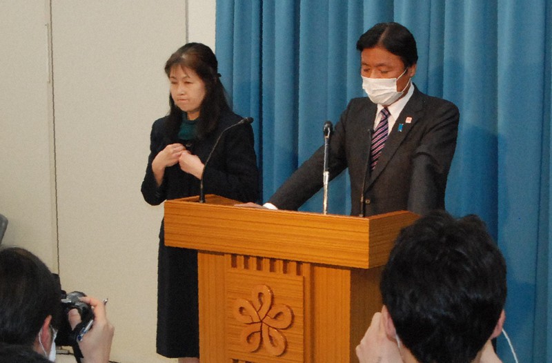 小川洋・福岡県知事(右)の横に立ち貴社会見の内容を伝える手話通訳者=福岡市博多区で2020年4月7日午後10時18分、中里顕撮影