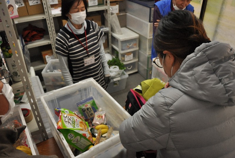 受け取った食品をバッグに詰める母親(右)。ボランティアスタッフが「頑張って」と送り出した=東京都江戸川区の「フードネット江戸川」で2020年4月9日、五十嵐朋子撮影