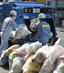 A pair of trash collectors, with masks on their faces, is seen loading up bags of waste onto their truck in Tokyo on April 24, 2020, in this partially modified image. (Mainichi/Yujiro Futamura)