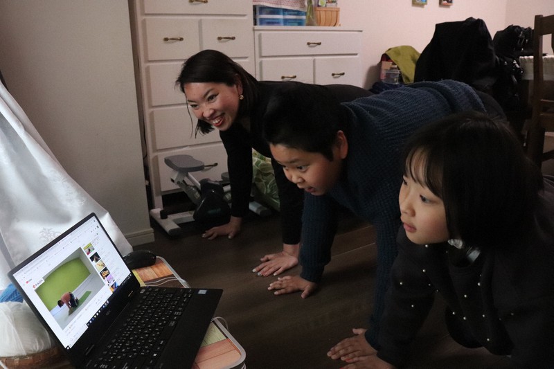 地域限定SNSアプリ「ピアッザ」の矢野晃平社長の運動動画を見ながら体を動かす木村千代子さん(左)と子どもたち=東京都中央区で2020年4月20日、後藤豪撮影