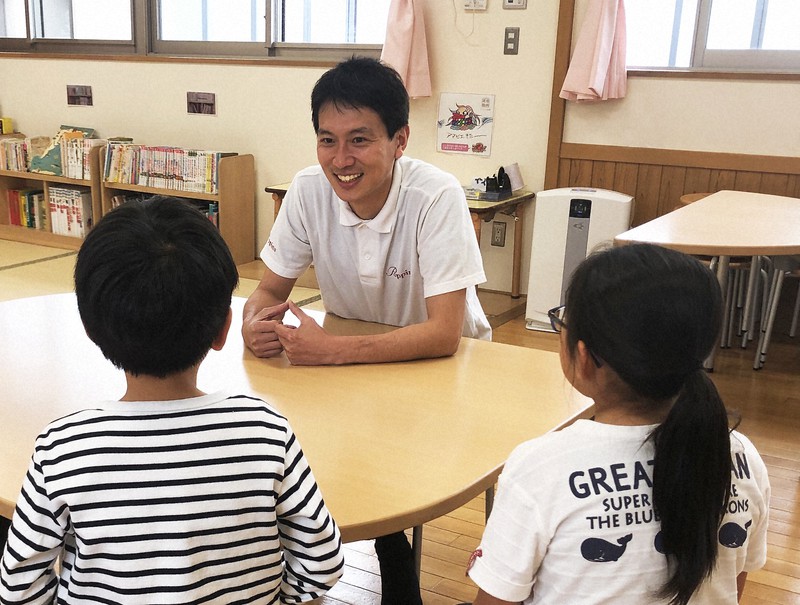 学童クラブで子どもたちと話す岡田一紀さん(奥)=ポピンズ提供