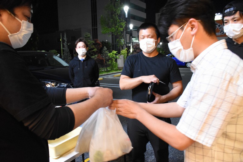 「チャリティーまぜそば」を受け取る男性(右)=前橋市古市町「和えそば・らーめん胡麦」駐車場で、2020年5月2日午後8時27分、川地隆史撮影