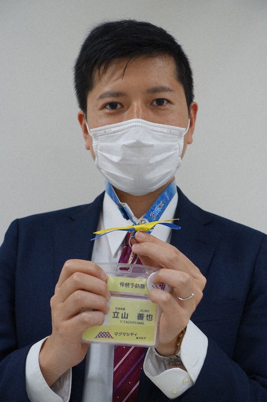 青色と黄色のリボンを身につける考案者の立山さん