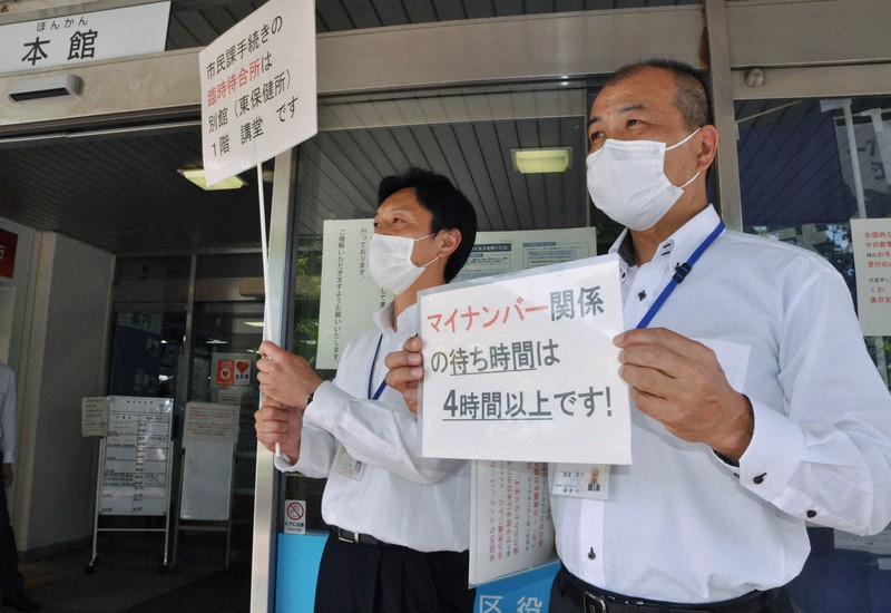 マイナンバーの暗証番号の設定に来る人が多く、「4時間待ち」を知らせる紙を持つ区役所職員=福岡市東区役所で2020年5月8日午後2時56分、平塚雄太撮影
