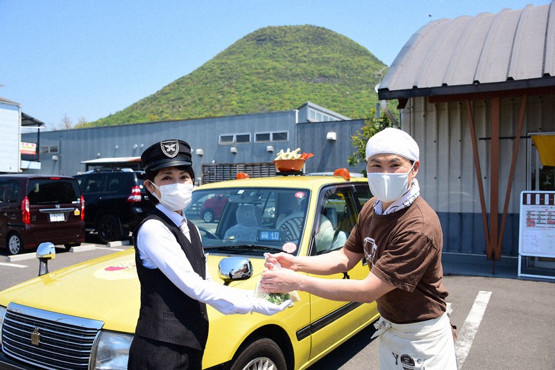 うどんタクシーのドライバーに配達用のうどんを手渡す山下義高さん(右)=香川県丸亀市飯野町で、潟見雄大撮影