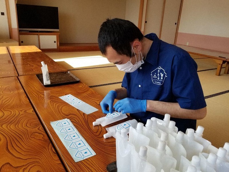 詰め替え用次亜塩素酸水のラベル貼り付け作業をする利用者=障害者就労支援法人「あおぞら」提供