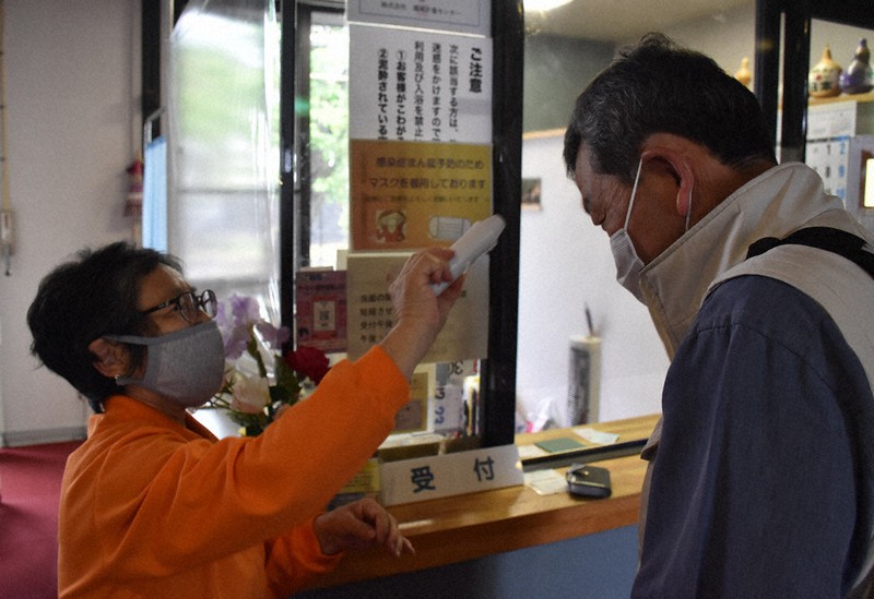 入浴受け付けの際、体温測定をする施設スタッフ(左)=山梨県甲斐市で