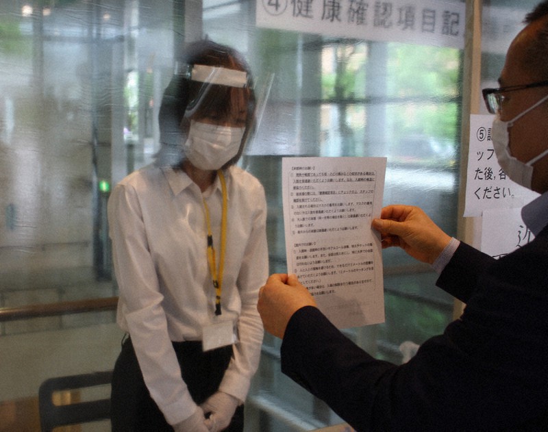 入場前に健康確認の用紙を受付の係員(左)に示す。係員はフェースシールドを着用し、来場者との接触を避けるため透明な板で隔てられている=広島市中区の広島県立美術館で15日午後2時24分、宇城昇撮影