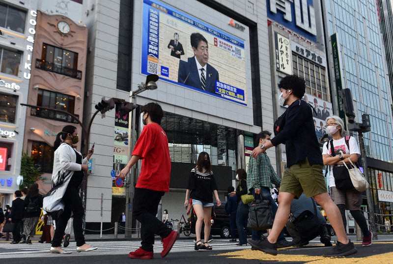 安倍晋三首相が緊急事態宣言全面解除を表明するニュースが流れる大型ビジョンの下を行き交うマスク姿の通行人ら=東京都新宿区で25日午後6時5分、滝川大貴撮影