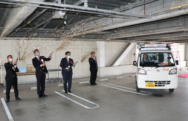 クラッカーを鳴らして脇本さんの車を見送る近商ストアの上田尚義社長(左から3人目)=奈良県広陵町馬見中4のエコール・マミで、稲生陽撮影
