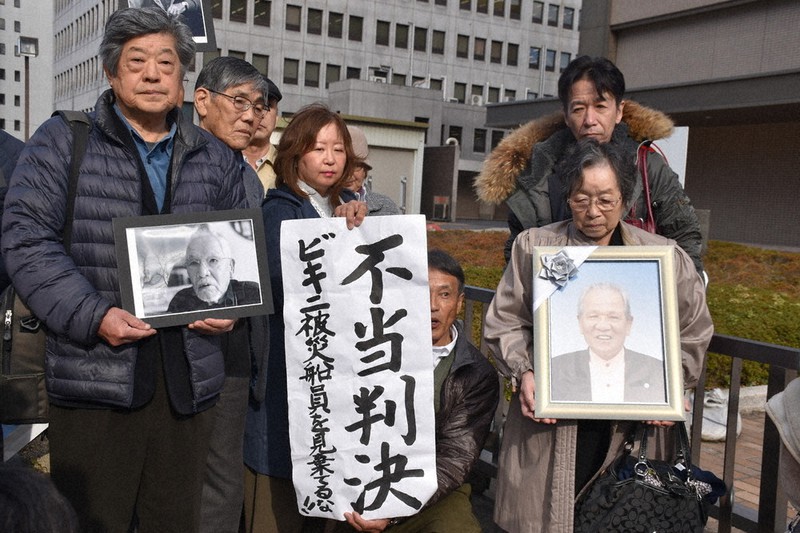 控訴審判決後に「不当判決」と書かれた紙を掲げる支援者。亡くなった元船員の写真を手にした遺族らは悔しさをにじませた=高松高裁前で2019年12月12日、松原由佳撮影