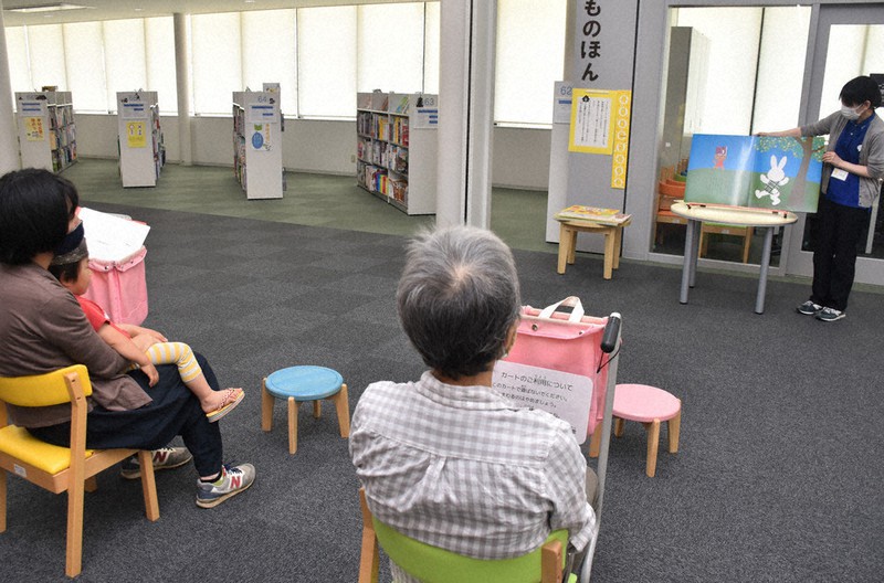 図書館職員(右奥)の読み聞かせに耳を傾ける親子連れ=山形県東根市で