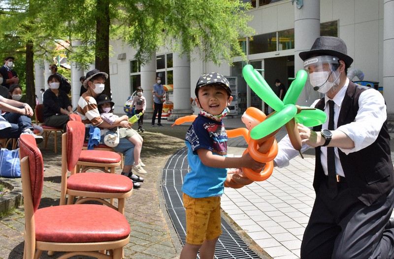 即興で作ったバルーンアートを子供に手渡すJinさん。観客に近付く時はマスクに加えフェースシールドを着けた=阿賀野市のサントピアワールドで2020年6月7日午後1時16分、井口彩撮影