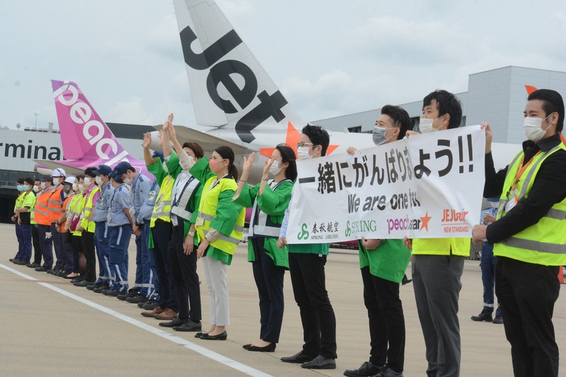 「一緒にがんばりましょう!!」と書かれた横断幕を手に、出発便を見送るLCC各社のスタッフ=成田空港で2020年5月31日午前11時50分、中村宰和撮影