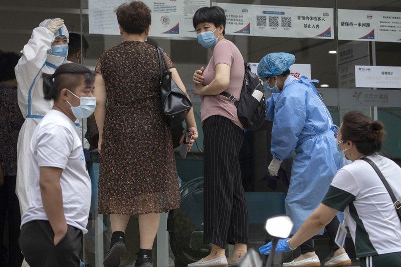 新型コロナウイルスの感染拡大を受け、PCR検査を受けるため訪れた住民らを防護服姿で迎える医療従事者ら=北京市で2020年6月17日、AP