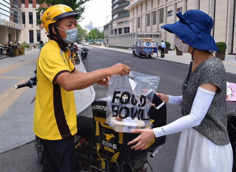 電動バイクから商品を取り出し、注文主に手渡す出前配達員=北京市内で8日午前、赤間清広撮影