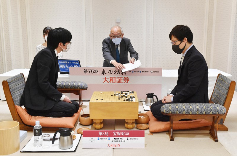 第75期本因坊決定戦七番勝負第3局で、開封した本因坊文裕(右)の封じ手を読み上げて示す立会の坂口隆三九段(中央)。左は挑戦者の芝野虎丸名人=兵庫県宝塚市の宝塚ホテルで2020年6月23日午前9時5分、北村隆夫撮影