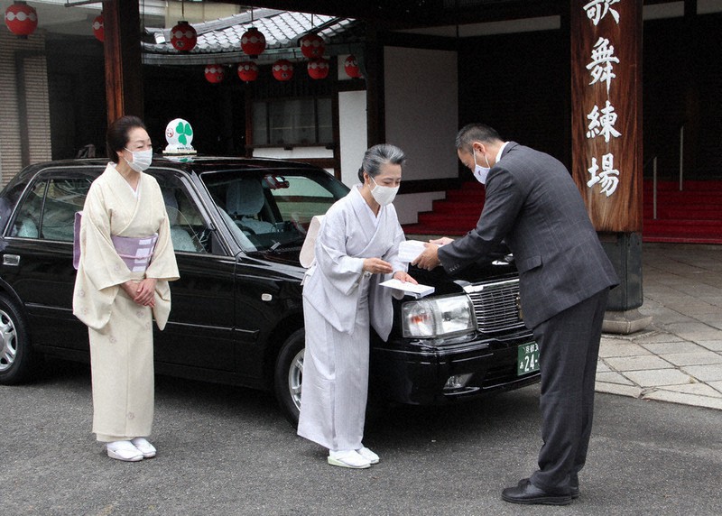 弥栄自動車の粂田晃稔副社長(右)からタクシー利用券を受け取る祇園甲部組合の杉浦京子さん(中央)=京都市東山区の祇園甲部歌舞練場で、福富智撮影