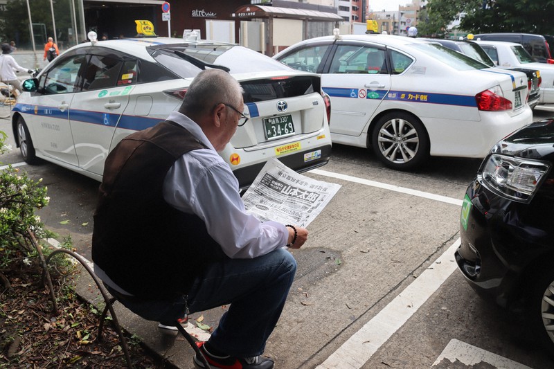 選挙公報を読む個人タクシーの運転手。コロナの影響で乗客はすっかり減ったという=東京都豊島区のJR巣鴨駅前で2020年6月23日午後1時23分、金子淳撮影