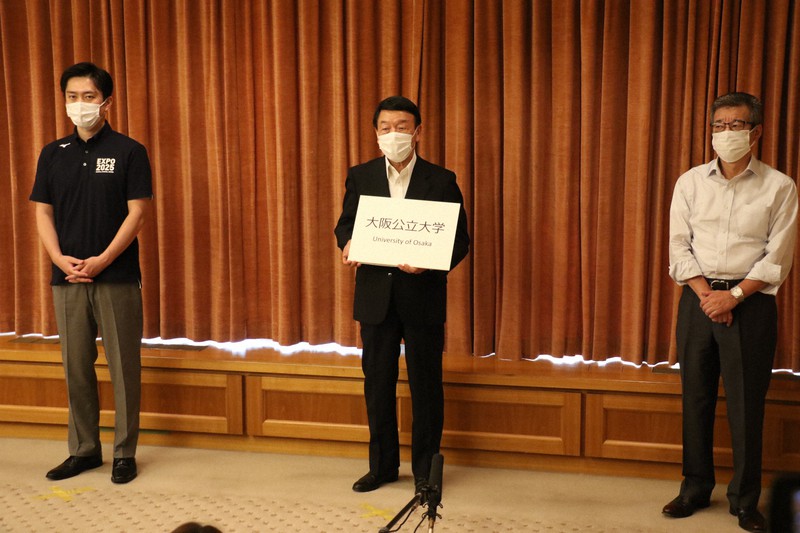 新大学の名称が「大阪公立大学」に決まり、ボードを掲げる公立大学法人大阪の西沢良記理事長(中央)=大阪市役所で2020年6月26日午後4時22分、野田樹撮影