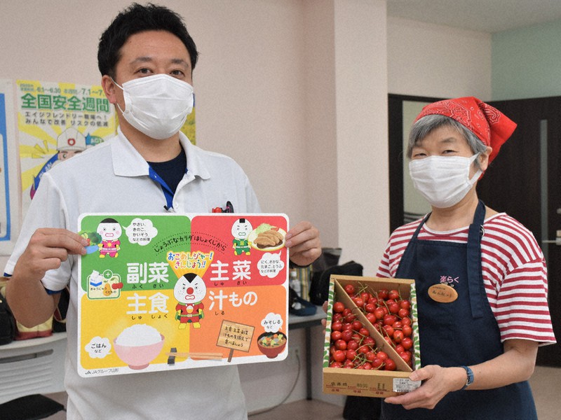 JAやまがたおいしさ直売所落合店の堀江店長(左)から提供されたサクランボを受け取る地域食堂「楽」を運営する西上さん=山形市で