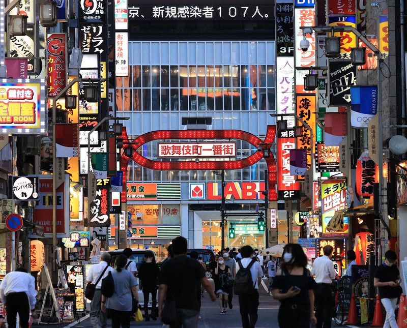 東京都の新規感染者が107人確認されたことを知らせるニュースが電光掲示板に表示される中、新宿・歌舞伎町を行き来する人たち=東京都新宿区で2020年7月2日午後6時50分、梅村直承撮影