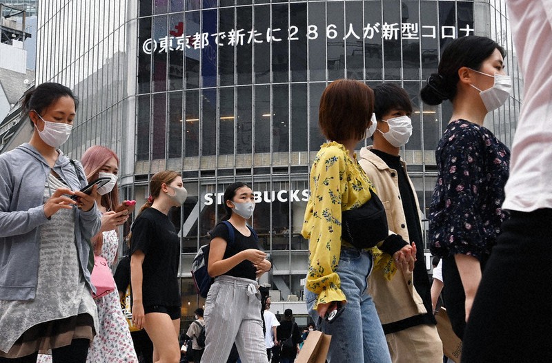 都内で過去最多の286人感染を伝えるニュースが流れる中、マスクを着けて渋谷のスクランブル交差点を行き交う大勢の人たち=東京都渋谷区で16日、大西岳彦撮影