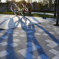 夕日に照らされ影が伸びる日本オリンピック委員会（JOC）の前に設置された五輪マーク。東京五輪が1年延期されたことで、スポンサー企業には困惑が広がっている＝東京都新宿区で2020年3月23日午後4時54分、大西岳彦撮影