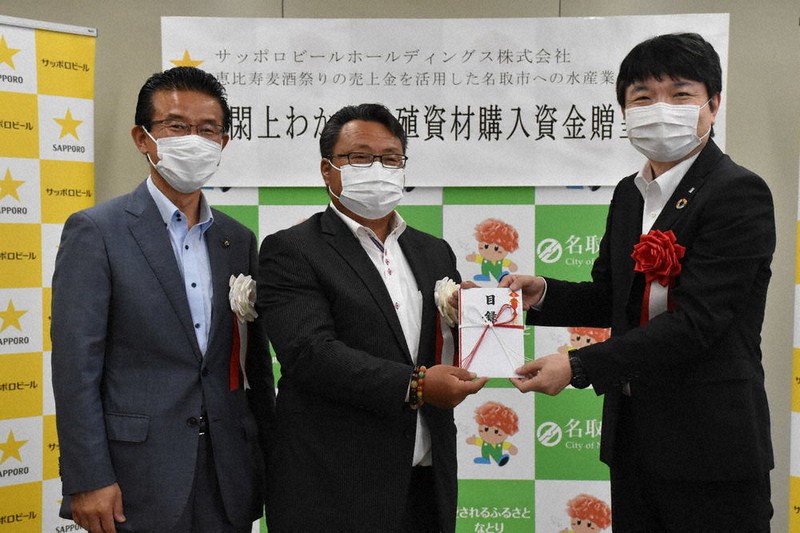 200万円を出雲浩行運営委員長(中央)に手渡す掃部晃工場長(右)と宮城県の山田司郎・名取市長