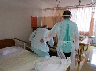 新型コロナウイルスのクラスター(感染者集団)が発生した大阪府内の高齢者施設で、ガウンやフェースシールドを身につけて利用者を介護する職員(右)=2020年8月18日(同施設提供)