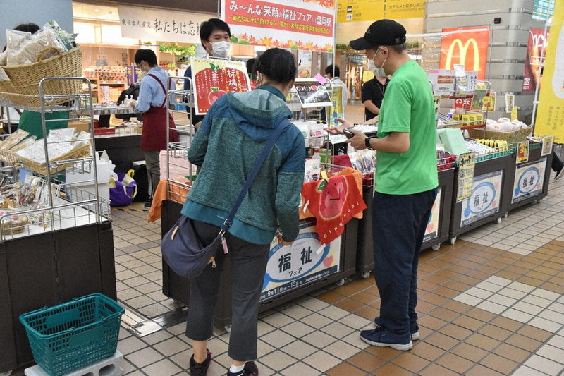 ドライフルーツの試食品を客に渡し、説明する平野健さん(右)=盛岡市盛岡駅前通で