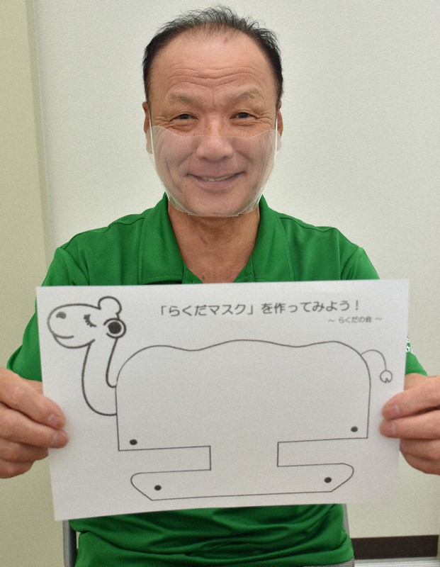 「らくだマスク」の型紙を掲げる前島和雄所長。着用しているのは、これで作った透明マスク=鳥取市富安2で、阿部絢美撮影