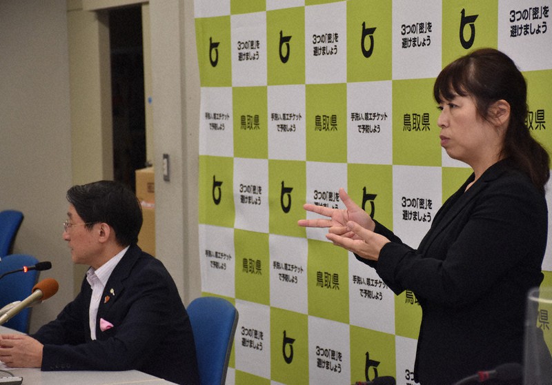 記者会見する平井伸治・鳥取県知事(左)の横に立つ手話通訳者。県内で初めて新型コロナのクラスター(感染者集団)が発生したことを伝えた=同県庁で12日、阿部絢美撮影