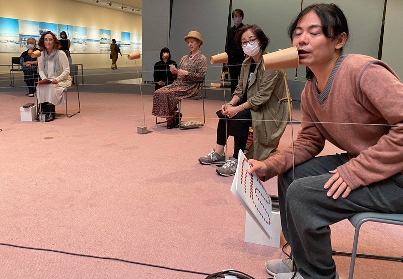会場に張り巡らされた糸でんわを試す、詩人のカニエ・ナハさん(右)。声が細いワイヤを震わせる=東京都港区で26日、小国綾子撮影