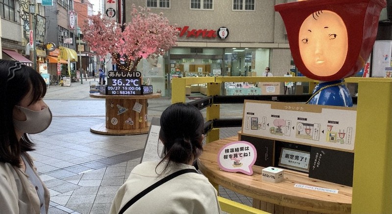 商店街に設置された検温ステーション。奥のモニターに結果が映し出される