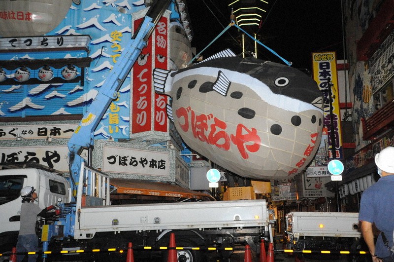 クレーンにつるされて撤去される、づぼらやの名物看板「ふぐちょうちん」。後ろに写るのは通天閣=大阪市浪速区で9月3日午前1時13分、澤俊太郎撮影