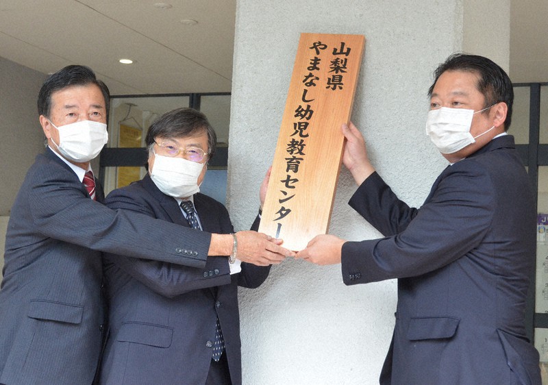 山梨県やまなし幼児教育センターの看板を掛ける長崎幸太郎知事(右)と、山梨大の島田真路学長(中央)、県立大の清水一彦学長=2020年10月1日、梅田啓祐撮影