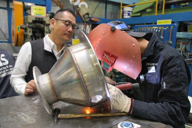 工場設備向けの金属部品を溶接する若手社員を見守る山田茂・山田製作所会長(左)。部品の受注は減少が続く=大阪府大東市で9月23日、宇都宮裕一撮影