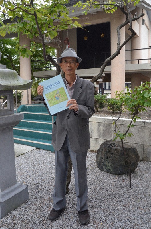 大沢地区のシンボルの神社で新刊を手にする北川司郎さん。右下は彦根藩主がタカ狩りの際に使ったとされる「井伊公の腰掛け石」=彦根市平田町の大沢鳴宮天満宮で2020年9月29日午前9時39分、伊藤信司撮影