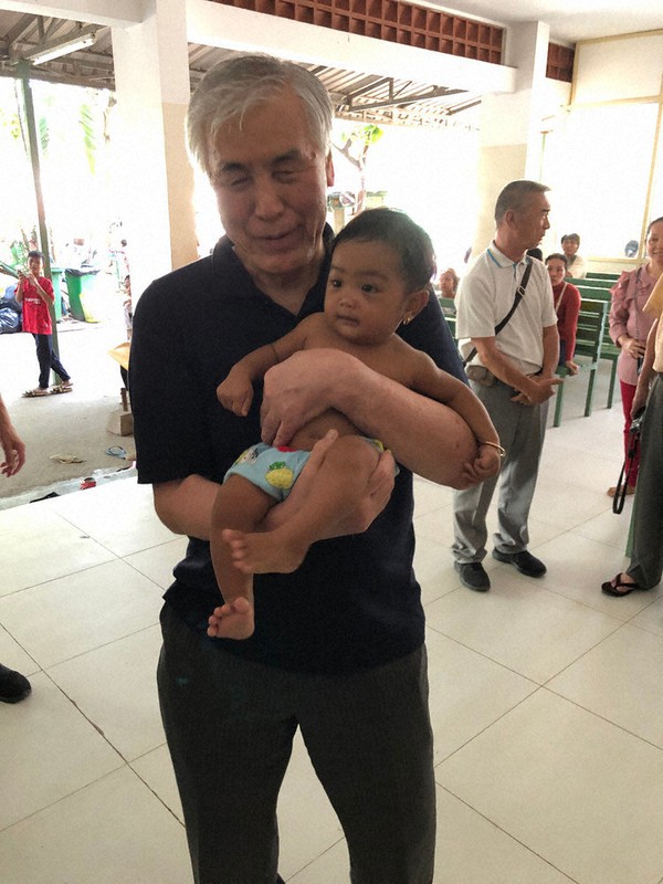 カンボジアを訪れ、ヒカリカナタ基金の支援で目の手術を受ける幼児を抱く竹内昌彦さん=竹内さん提供