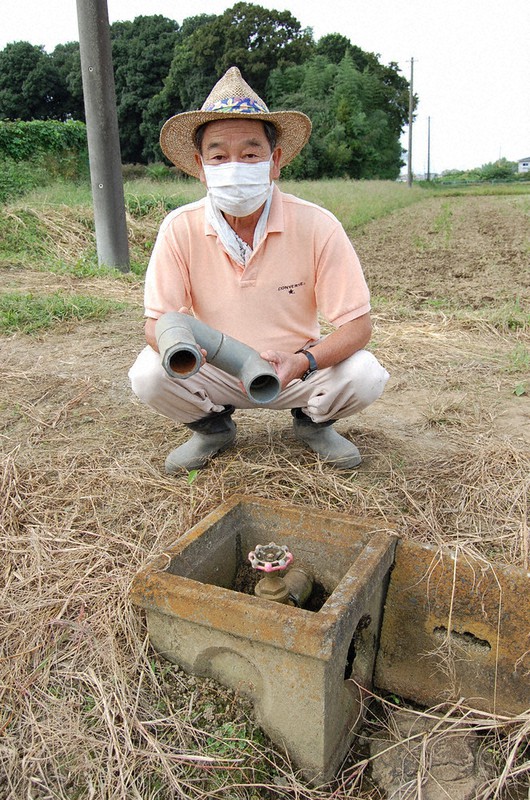 盗まれたものと同型の金属製バルブが設置された場所で、切断された樹脂製配管を持つ吉田善一組合長=埼玉県白岡市内で2020年10月6日、古賀三男撮影