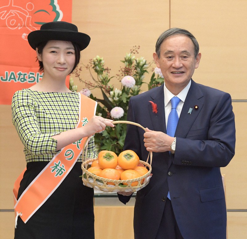 「奈良の柿PRレディ」から贈呈された柿を手に笑顔で記念写真に納まる菅義偉首相(右)=首相官邸で2020年10月15日午後2時14分、竹内幹撮影