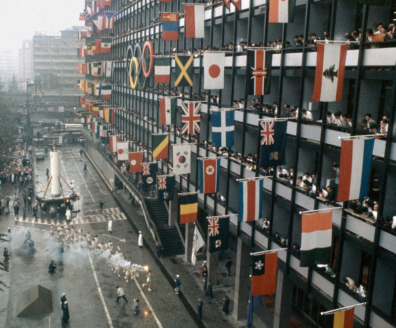 報道写真展で展示する1964年東京五輪大会で旧東京都庁の窓から歓迎の各国旗が掲げられる中、到着する聖火ランナーの写真=同年10月7日撮影